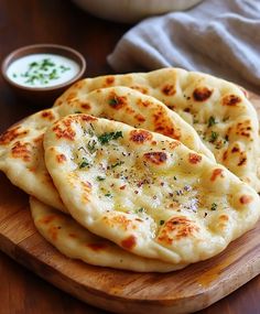 three pita breads on a cutting board with dip sauce in the back ground