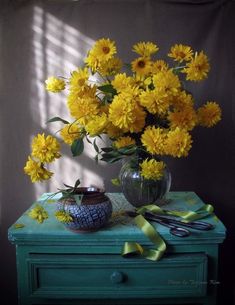 a vase filled with yellow flowers sitting on top of a green table next to scissors