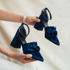 the woman is holding two pairs of blue high heeled shoes with bows on them