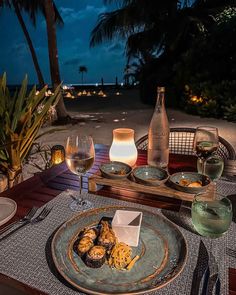 an outdoor dining table set for two with wine, food and glasses on it at night