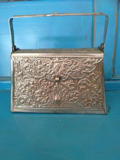 This Stunning Intricate Pewter Metal Mini Bag has intricate embossed pattern and graphics on it. It is velvet lined and has a sturdy latch and swivel top handle. I honestly do not know the era could be earlier than 60s and the art is of Asian Origin. Regardless, it's quite the statement piece and in great condition! Measurements: Top Width 5.5" Bottom Width 6.5" Handle 9" Depth 1.75" to 2.5" at Bottom Height 4" Vintage Embossed Satchel Bag, Vintage Rectangular Engraved Bag, Vintage Rectangular Engraved Bags, Vintage Engraved Satchel Bag, Vintage Engraved Rectangular Bag, Vintage Engraved Bags As Gifts, Antique Rectangular Bags For Gifts, Vintage Silver Rectangular Bag, Antique Rectangular Gift Bags