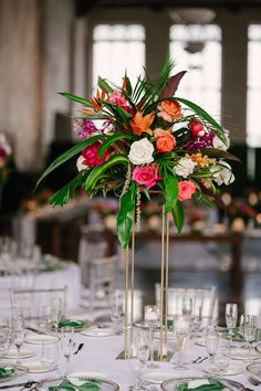 a tall vase filled with lots of flowers on top of a white table covered in glasses