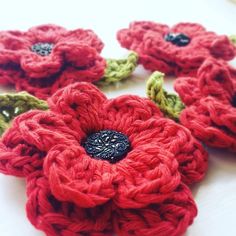 crocheted red flowers with green stems and black centers sitting on a white surface