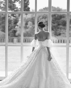 a woman in a wedding dress is looking out the window with her back to the camera