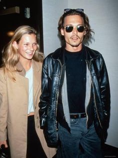 a man and woman standing next to each other in front of a wall wearing sunglasses