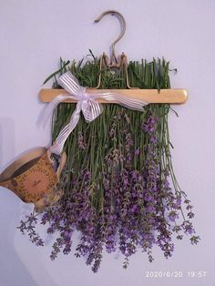 lavender flowers hang from a coat rack with a white bow on the top, and a watering can below