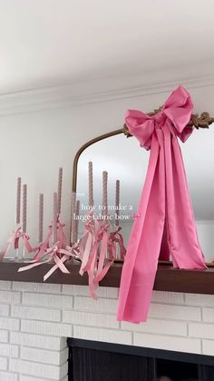 pink ribbons are tied to the mantle in front of a mirror with candles on it