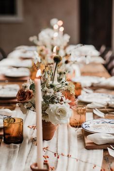 the table is set with candles, plates and flowers in vases on top of it