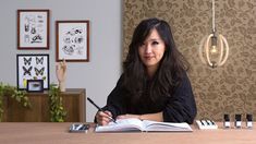 a woman sitting at a table with an open book in front of her and writing