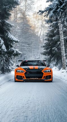 an orange and black sports car driving down a snow covered road in front of trees