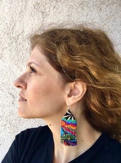 a woman with red hair wearing a pair of multicolored beaded earrings on her ear