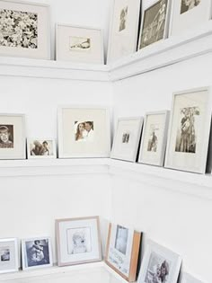 many framed pictures are on the wall above a shelf in a room with white walls