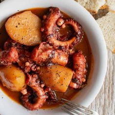 an octopus stew in a white bowl with bread on the side and a fork next to it