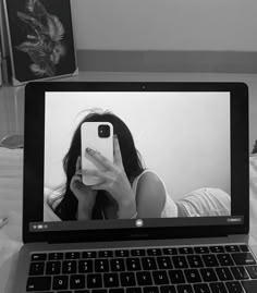 a laptop computer sitting on top of a bed with a woman taking a selfie