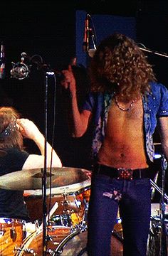 a man with no shirt on standing next to a drummer and another person holding a microphone