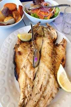 a white plate topped with grilled fish next to bowls of salad