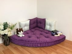 a purple round couch sitting on top of a wooden floor next to a vase with flowers