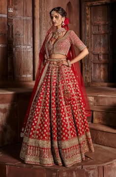 a woman in a red and gold bridal gown standing on a rug with flowers