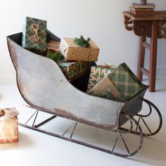 a sleigh filled with wrapped presents on top of a white floor next to a christmas tree