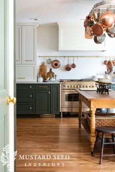 a kitchen with wooden floors and green cabinets, pots hanging from the ceiling over the stove