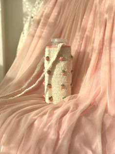 a crocheted purse sitting on top of a pink bed sheet next to a curtain