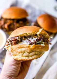 a hand holding up a sandwich with meat and cheese on it next to some dipping sauce