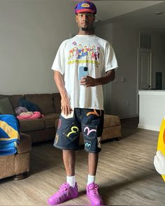 a man standing in front of a couch wearing shorts and a t - shirt with cartoon characters on it