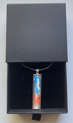 Abstract acrylic rectangle pendant necklace. Blue, white and orange abstract swirl set in a silver tray with matching 16 inch silver chain. Artistic Rectangular Necklace For Gifts, Artistic Rectangular Necklace For Gift, White Necklace With Rectangular Pendant For Gift, Rectangular Multicolor Necklaces As Gift, Multicolor Rectangular Necklace As Gift, Silver Oblong Necklaces For Gifts, Silver Oblong Necklace For Gift, Artistic Rectangular Pendant Necklace As Gift, Artistic Rectangular Pendant Necklace For Gift