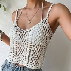 a woman wearing a white crochet tank top and denim shorts with her hand on her hip