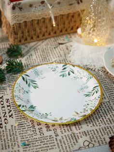 an empty plate sitting on top of a newspaper next to a glass vase and candle