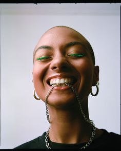 a woman with green eyeliners and chains on her mouth smiling at the camera