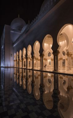 the interior of a large building with columns and arches reflecting in the water at night