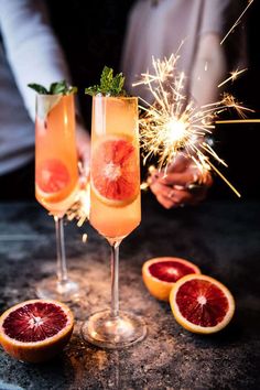 two glasses filled with liquid and garnished with sparklers on a table next to grapefruits