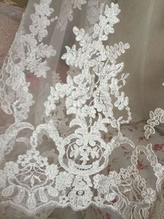 white lace with flowers on it is laying on the ground next to a piece of cloth