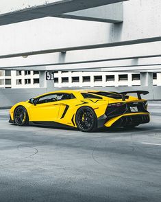 a yellow and black sports car parked in front of a white building with concrete flooring