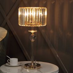 a table with a lamp on it next to a cup and saucer in front of a wall