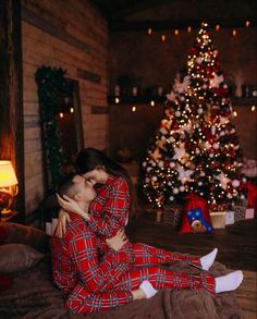 two people in pajamas sitting on a bed next to a christmas tree