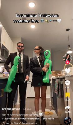 two people standing in a kitchen holding green blow - up balloons with ghost faces on them