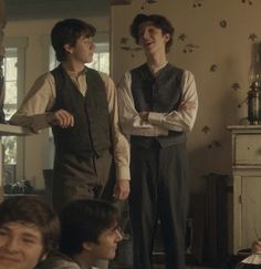 three young men standing next to each other in front of a dresser and table with papers on it