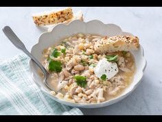 a white bowl filled with chicken and rice soup next to a piece of bread on a blue towel