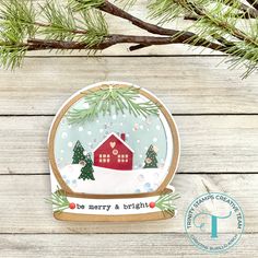 a christmas ornament with a red house and trees in the snow on a wooden background