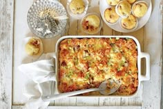 a casserole dish on a table with muffins and other food items