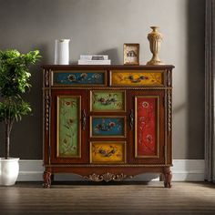 an ornate wooden cabinet with painted doors and drawers in a room next to a potted plant