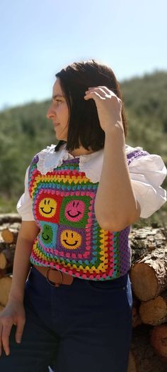 a woman wearing a colorful crochet bag sitting on top of a pile of logs