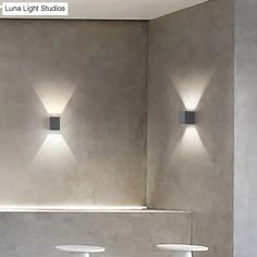 three lights are on the wall in a room with concrete walls and white flooring