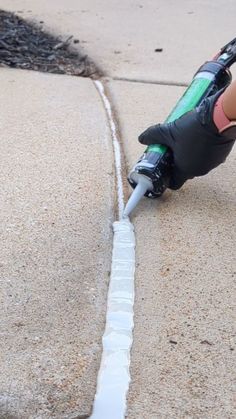 a person in black gloves is using a hose to fix a drain on the sidewalk