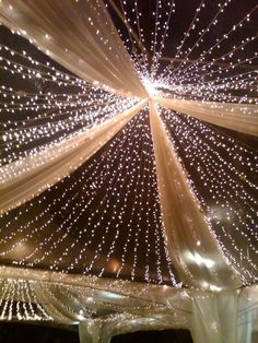 the ceiling is decorated with lights and drapes for an outdoor wedding reception at night