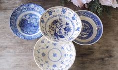 three blue and white plates sitting on top of a wooden table next to pink flowers