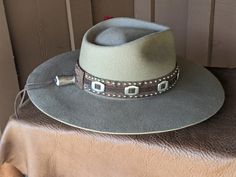 The Bandit is a stand out hat that captures the feeling of the American West. . The base of the hatband is distressed leather that is then layered with imprinted brown leather, bolo sliders and lots of nailspots. It is finished with this colorful feather combo. The brim of the LID custom hat body is 4" in diameter and the crown is 4.5". This is a stiff hat. Available in Putty or Pecan All hats are made to order. Allow up to 4 weeks for your hat to ship. Distressed Brown Hats With Short Brim For Country Events, Rustic Hat With Distressed Brown Curved Brim, Rustic Hat With Curved Brim In Distressed Brown, Rustic Hat With Distressed Brown Color And Curved Brim, Rustic Distressed Brown Hat With Curved Brim, Distressed Brown Fedora For Country Events, Rustic Distressed Brown Brimmed Hat, Western Style Brown Hat With Flat Crown, Distressed Brown Adjustable Hat For Western-themed Events