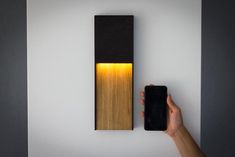 a hand holding a cell phone next to a wall light that has a wooden panel on it